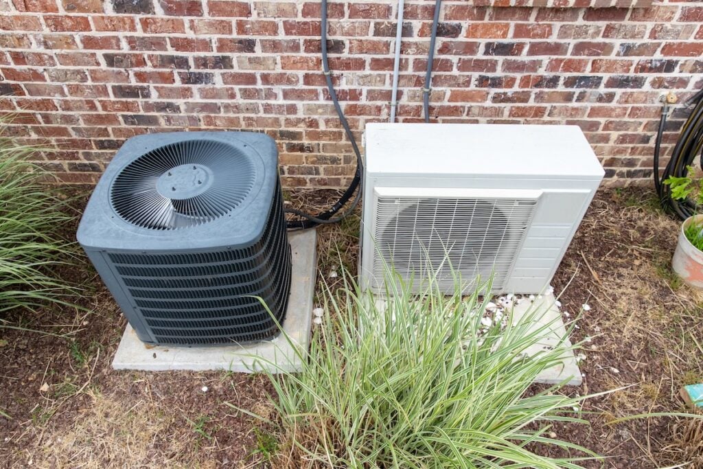 HVAC Air Conditioner Compressor and a Mini-split system together next to each other, next to a brick home.