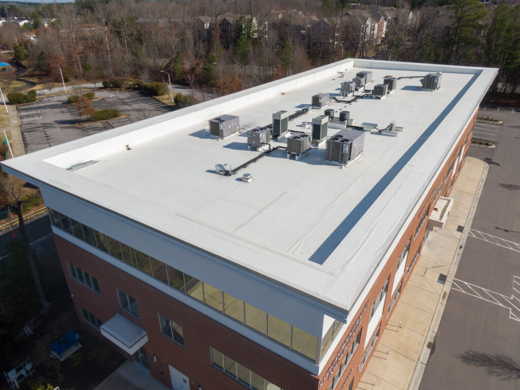 Square air-conditioning unit on the roof with a round fan. In the background gradually receding other units that are out of focus. On the right side light blue sky and commercial space.