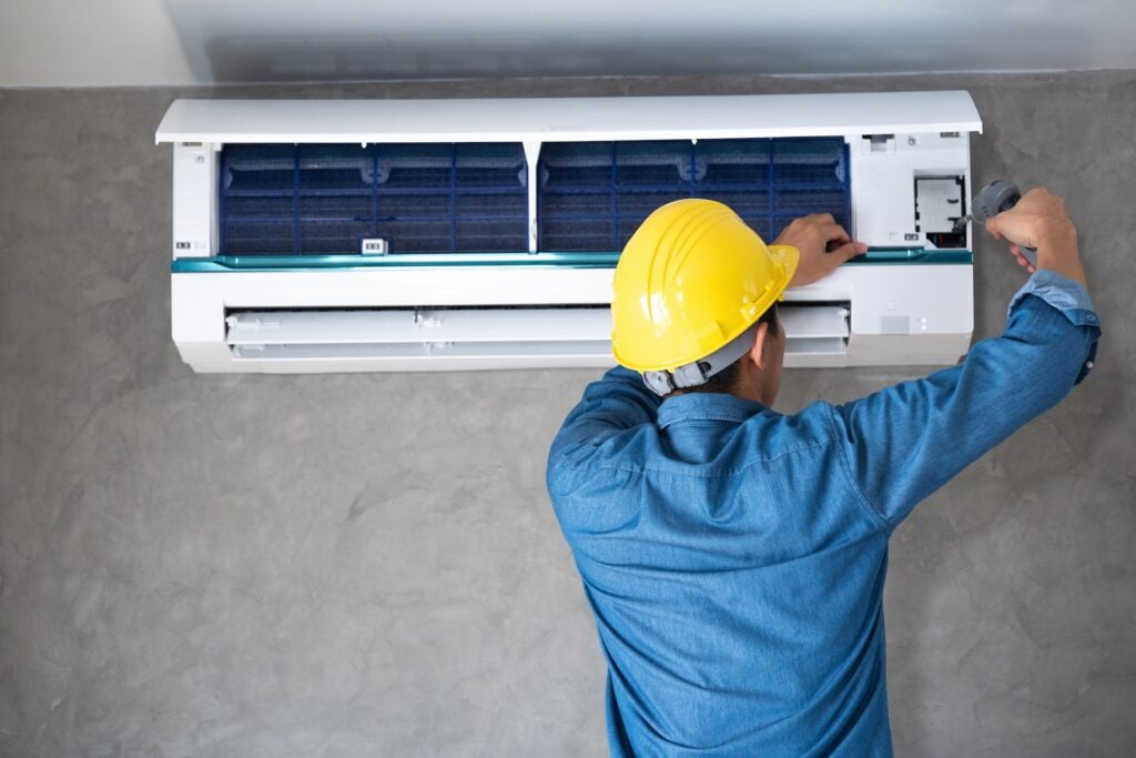 Technician man repairing ,cleaning and maintenance Air conditioner on the wall with screw driver in bedroom or office room.On site home service,Business ,Industrial concept. what is the $5000 rule for hvac?