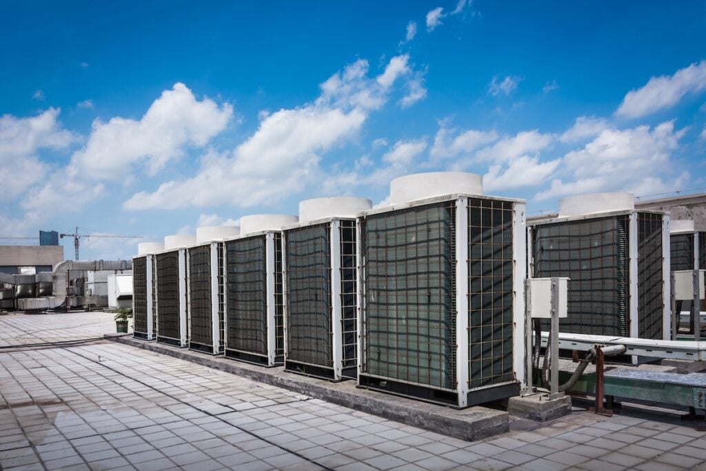 commercial hvac installation Square air-conditioning unit on the roof with a round fan. In the background gradually receding other units that are out of focus. On the right side light blue sky and commercial space.