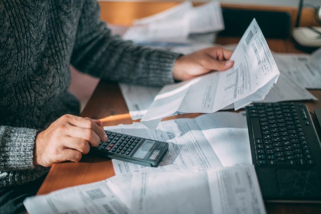 how to save money on heating bill Close-up of male hands with a utility bill, a lot of checks and a calculator on the table. The man considers the costs of gas, electricity, heating. The concept of increasing tariffs for services