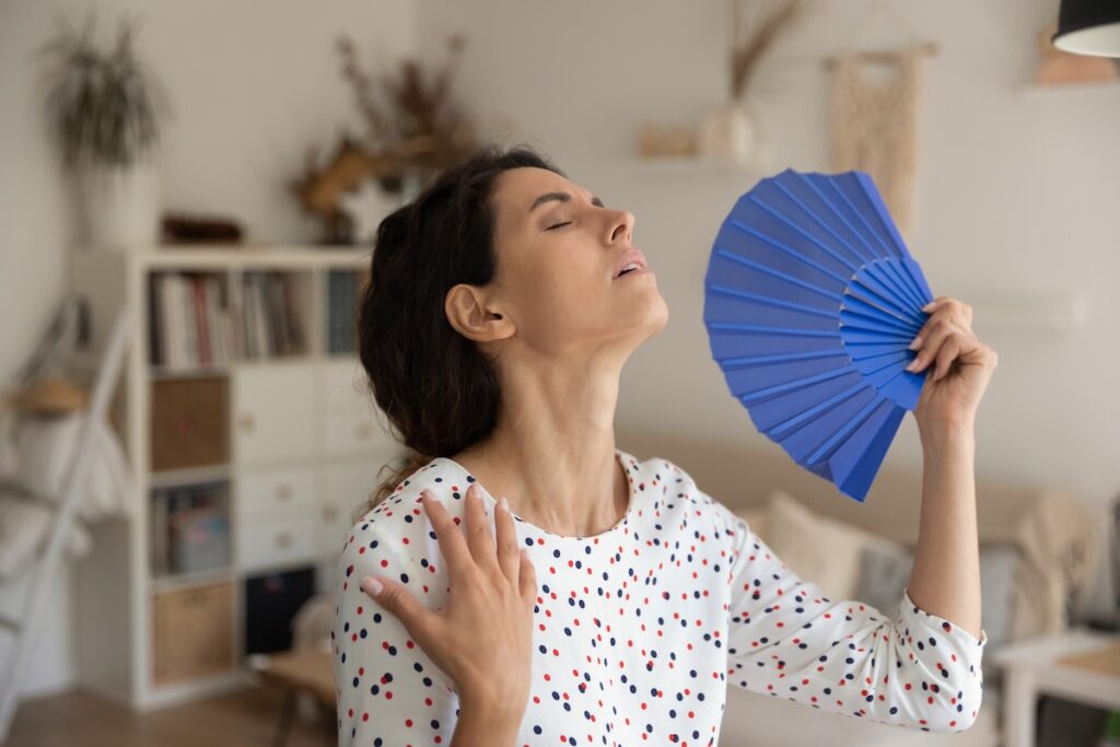 What a heat. Exhausted young female housewife suffer from extra hot temperature at home apartment wave herself use hand weaver. Overheated millennial woman cool air with paper fan miss air  conditioner how to reduce humidity in house