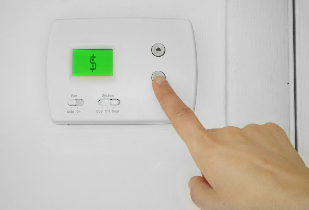 best hvac system for home Person adjusting a wall thermostat with dollar sign symbol on the display