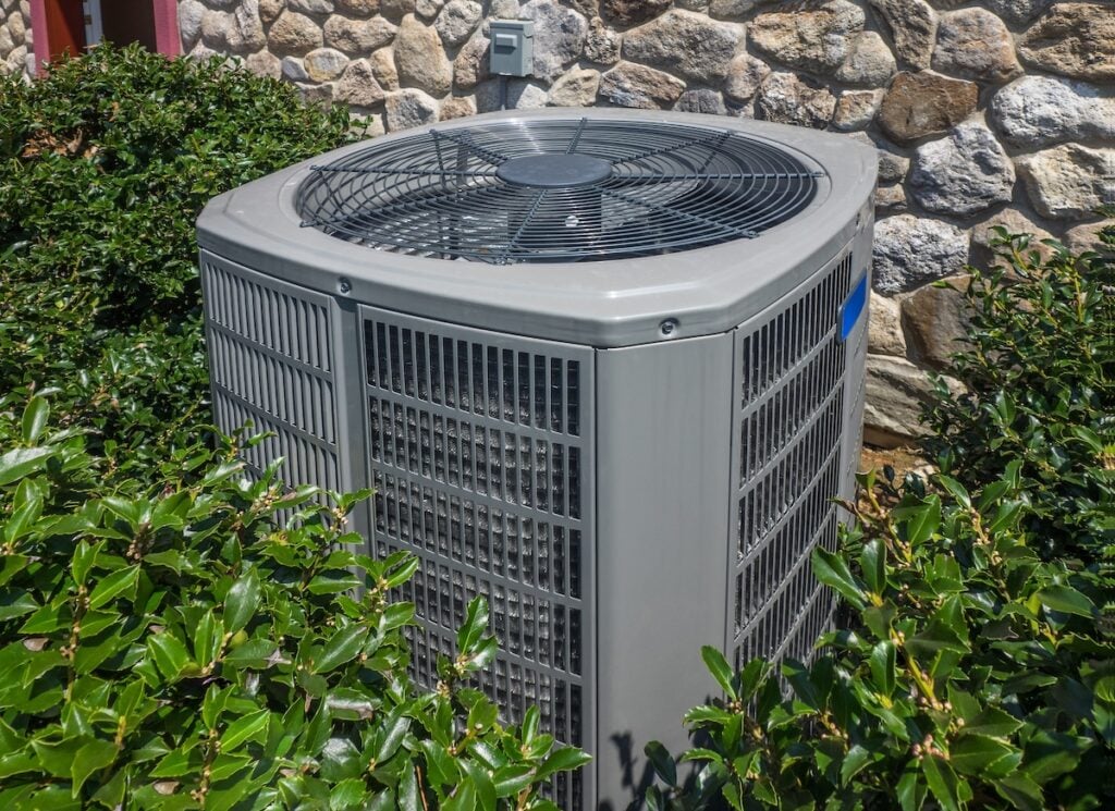 trane vs carrier Air conditioning and heating unit for a residential house hidden by holly