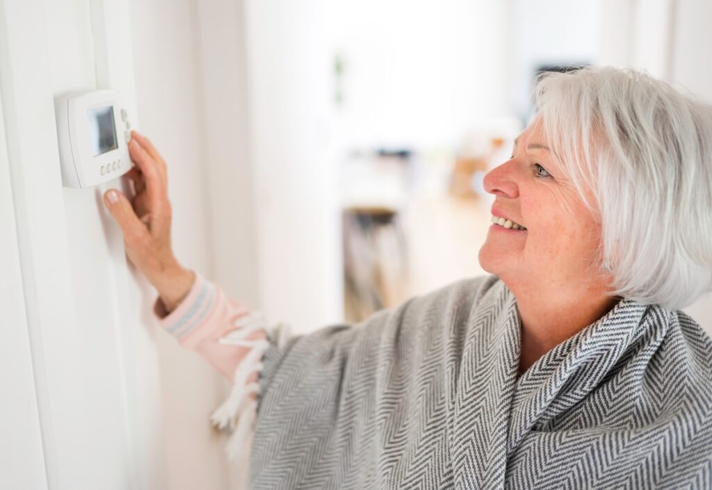 how to keep house warm in winter A Senior woman adjusting her thermostat at home