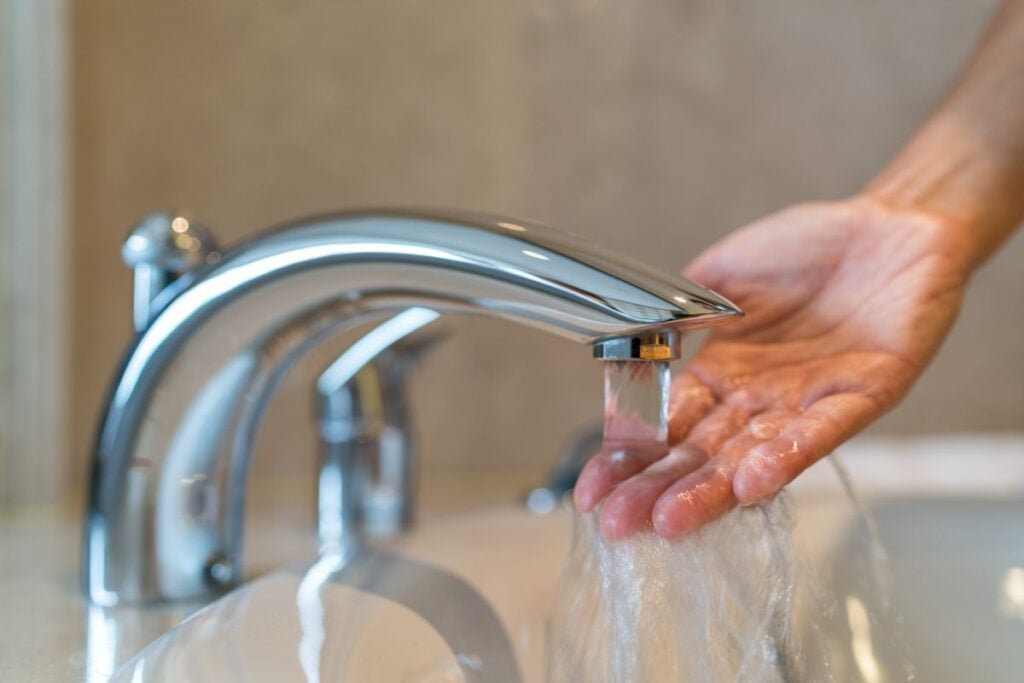 heating installation young woman checking water temperature with hand inside bathroom