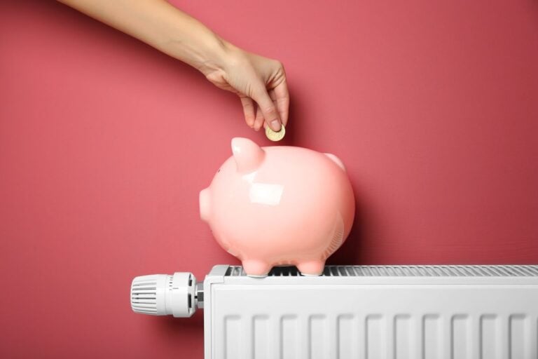 hvac repair cost modern energy saving thermostat hand saving coin inside piggy bank against red wall