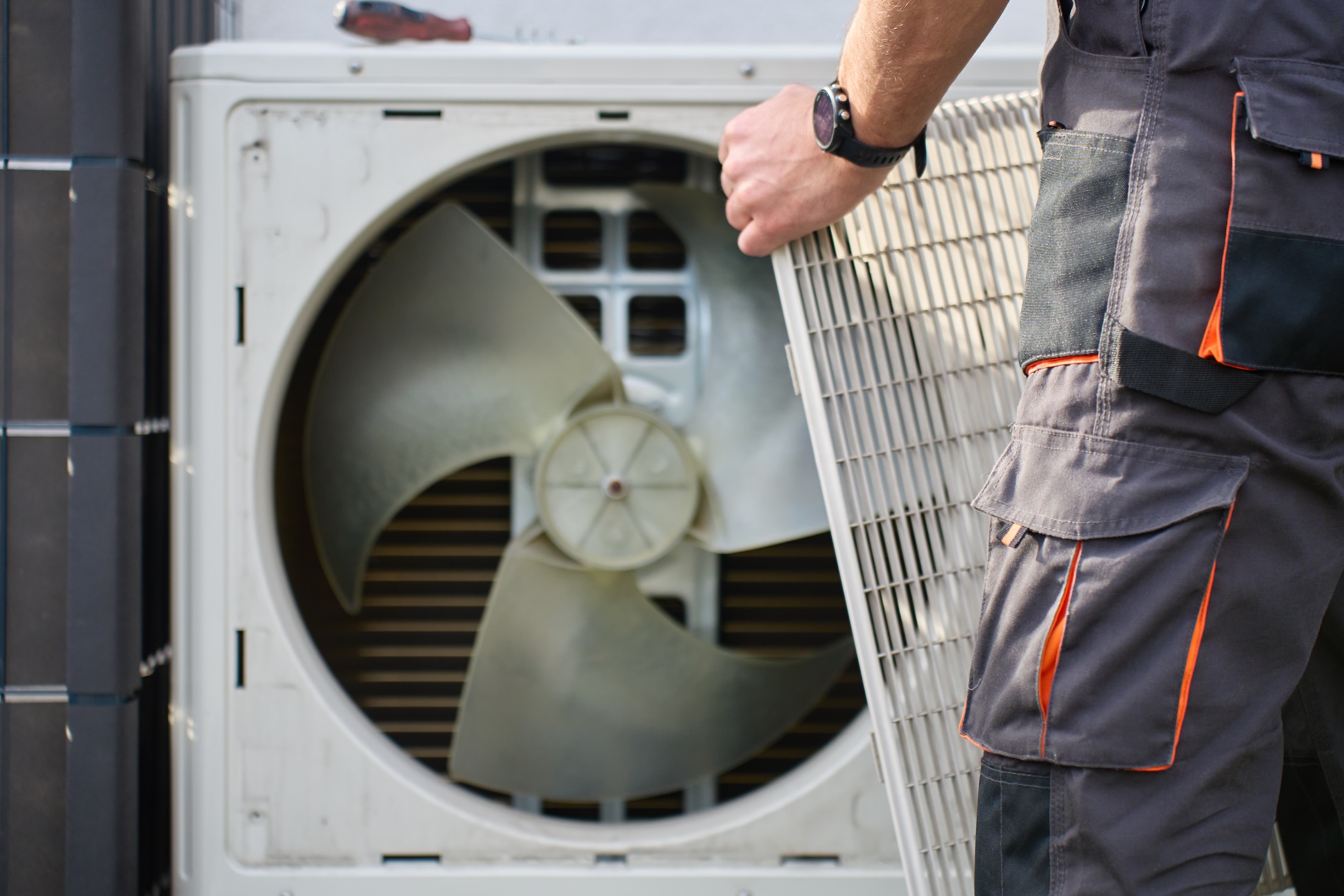 Technician removing front cover grille from outdoor heat pump unit during residential HVAC service.