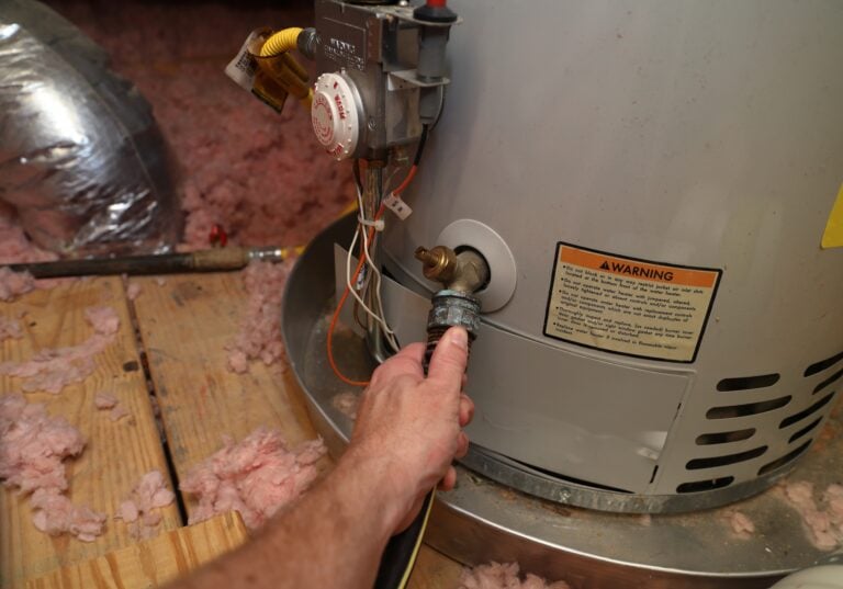 Hand attaches hose to a home water heater to perform maintenance