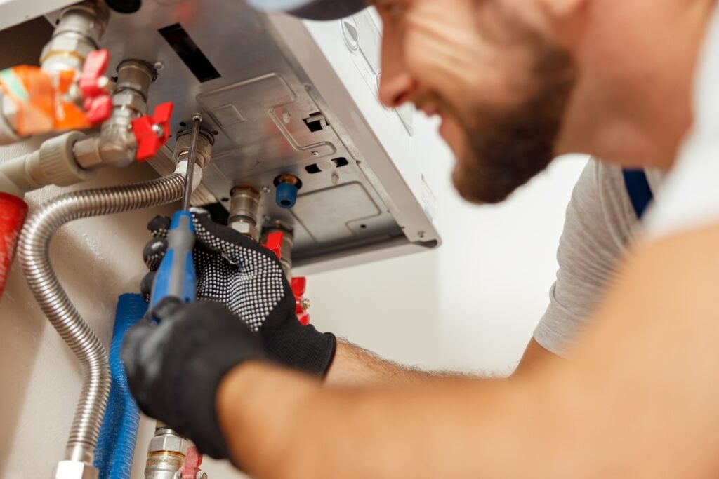 Plumber using screwdriver while installing new steel hot water central heating system in apartment