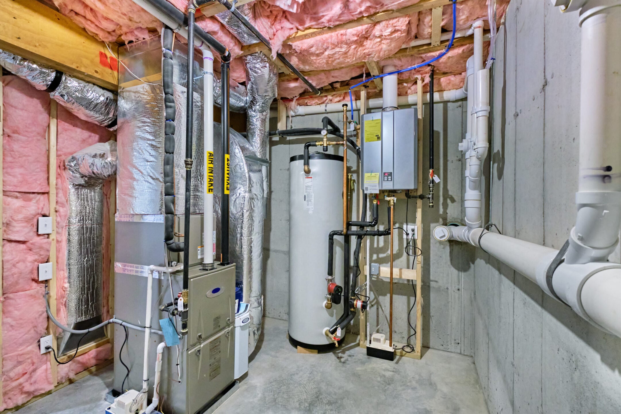 basement mechanical room with tankless water heater, storage tank, plumbing and heating systems