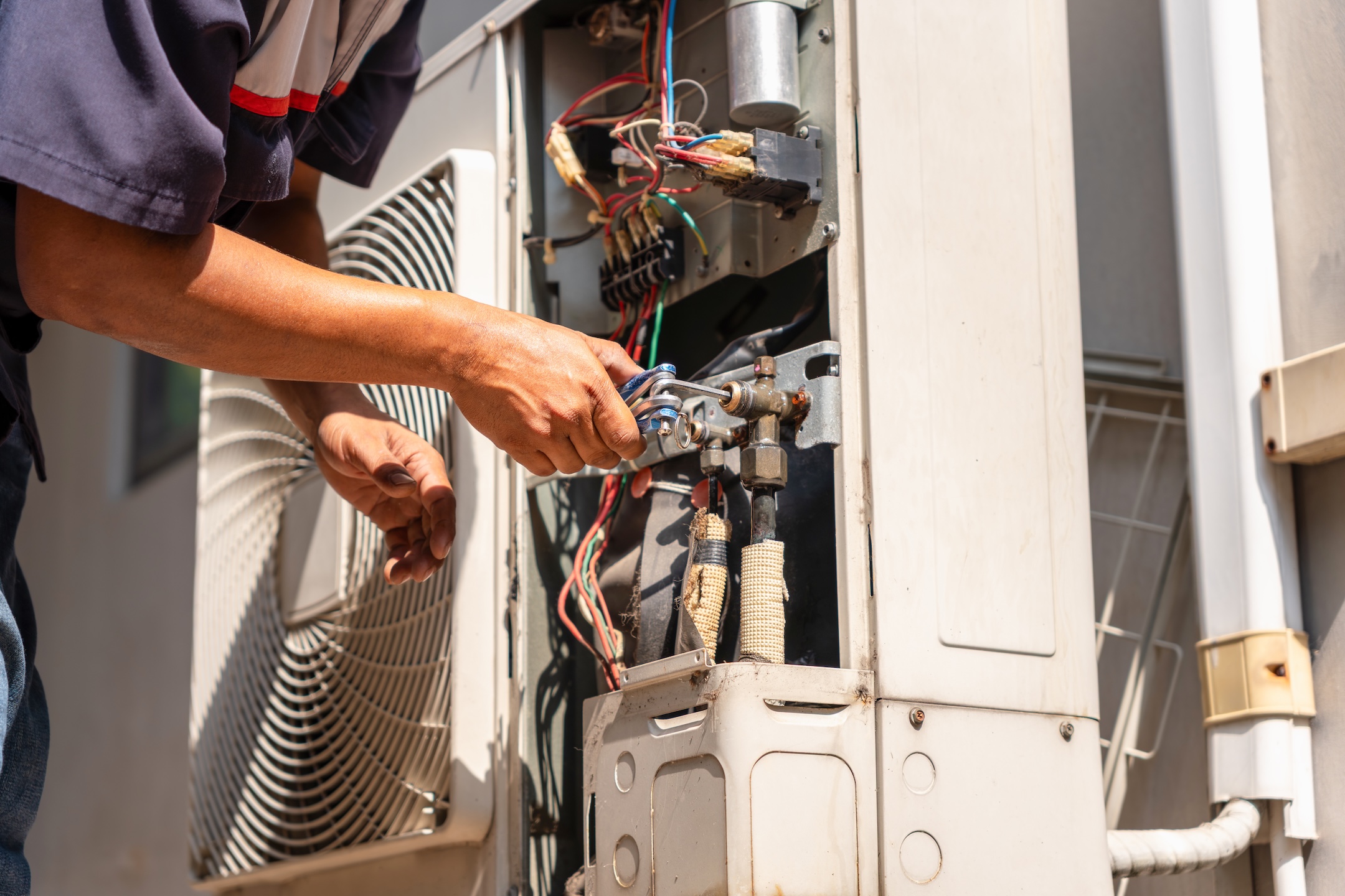 Technician man performing maintenance service on home air conditioning system, Worker hands using allen key to adjust valve on outdoor unit, HVAC contractor repairing a split system air conditioner
