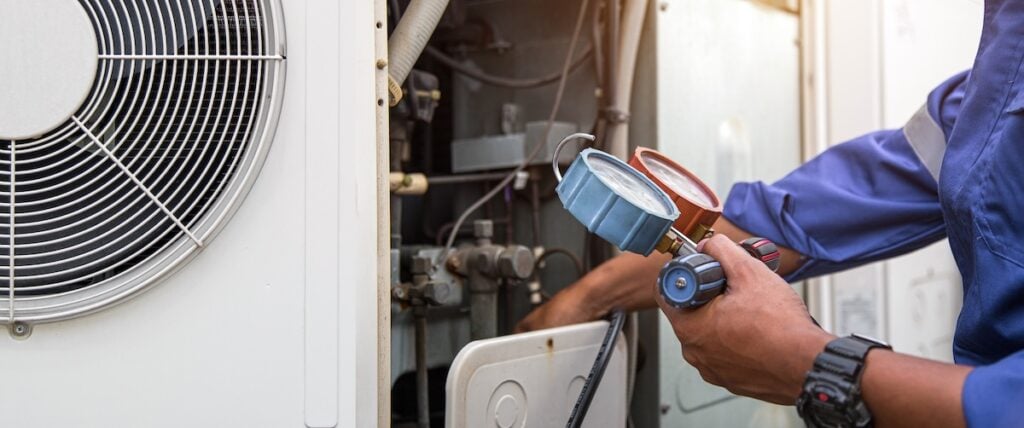 Heat and Air Conditioning, HVAC system service technician using measuring manifold gauge checking refrigerant and filling industrial air conditioner after duct cleaning maintenance outdoor compressor.